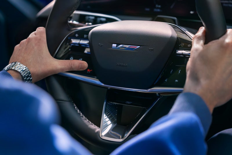 Close-up of a Man About to Press the V-Button on the 2026 OPTIQ-V Steering Wheel | Dossett Cadillac in HATTIESBURG MS